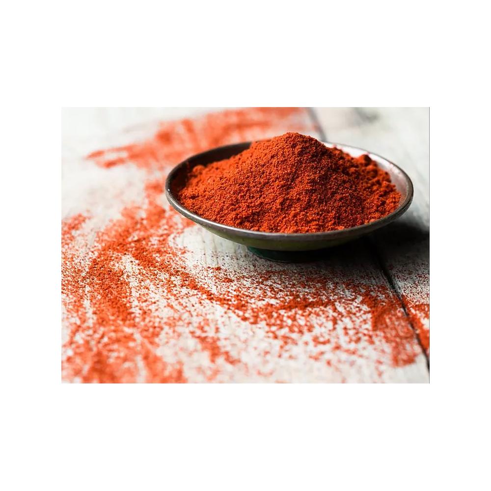 Close-up of fine red-orange li hing mui powder in a metal bowl with powder scattered on a white wooden surface
