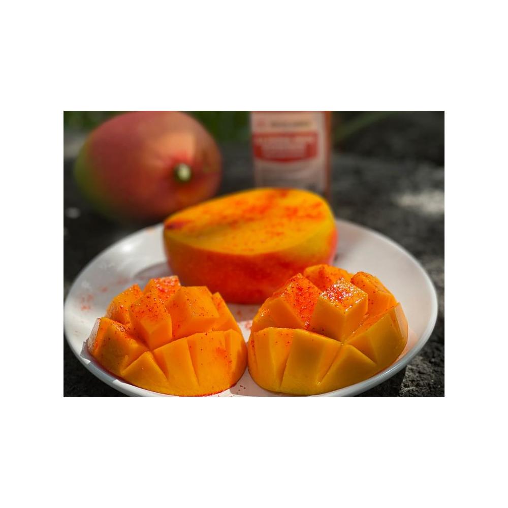 Sliced mango topped with red li hing mui powder on a white plate with a whole mango and li hing container in the background

