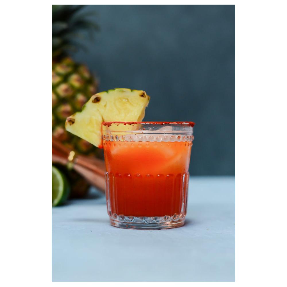 Glass of li hing mui margarita garnished with pineapple wedge and rimmed with red powder, set against a tropical background